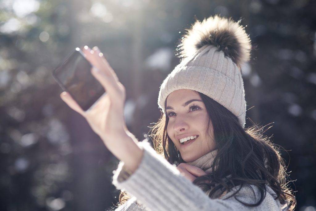 Portrait of smiling young woman taking selfie with smartphone in winter forest