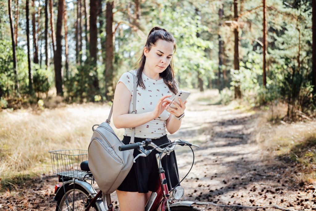 Best cycling apps. Bike Tracker. Young woman with backpack riding bike and looking in cell phone on