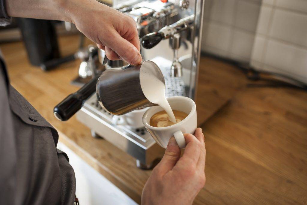 Cappuccino, man pouring milk froth in coffee cup