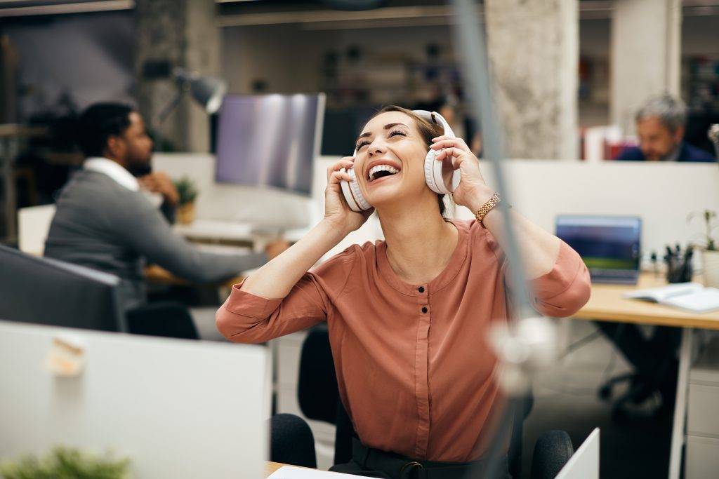 Carefree businesswoman enjoying in music over headphones in the office.