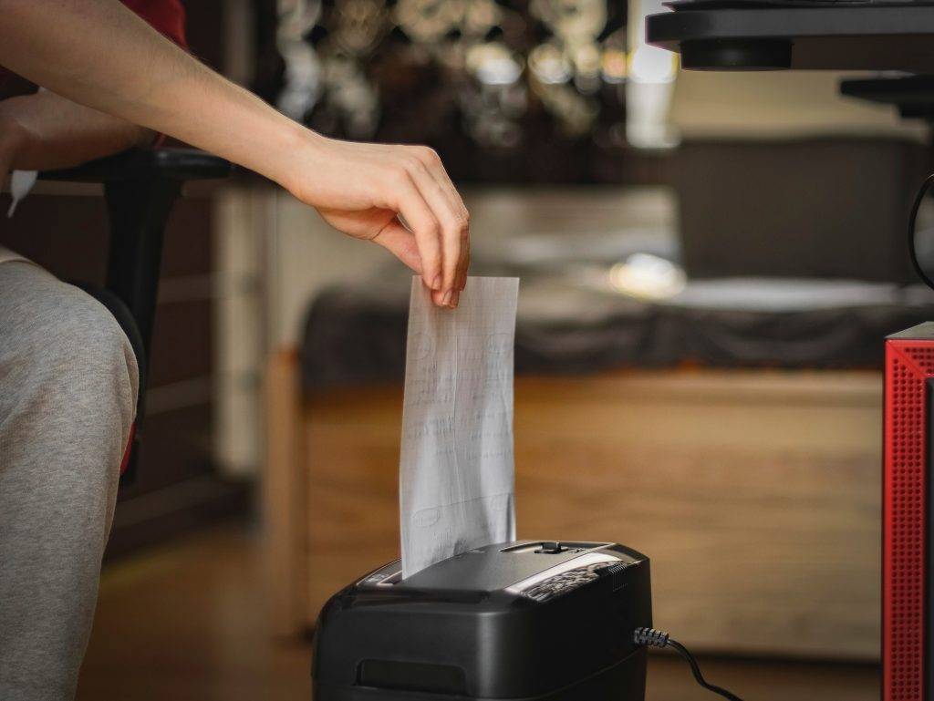 Caucasian young man inserts a sheet of paper for destruction in a black shredder