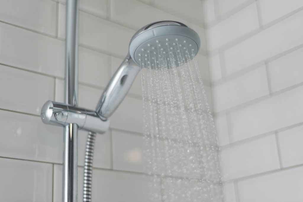Close-up of chrome shower, faucet, in the bathroom covered decorative ceramic tiles with white