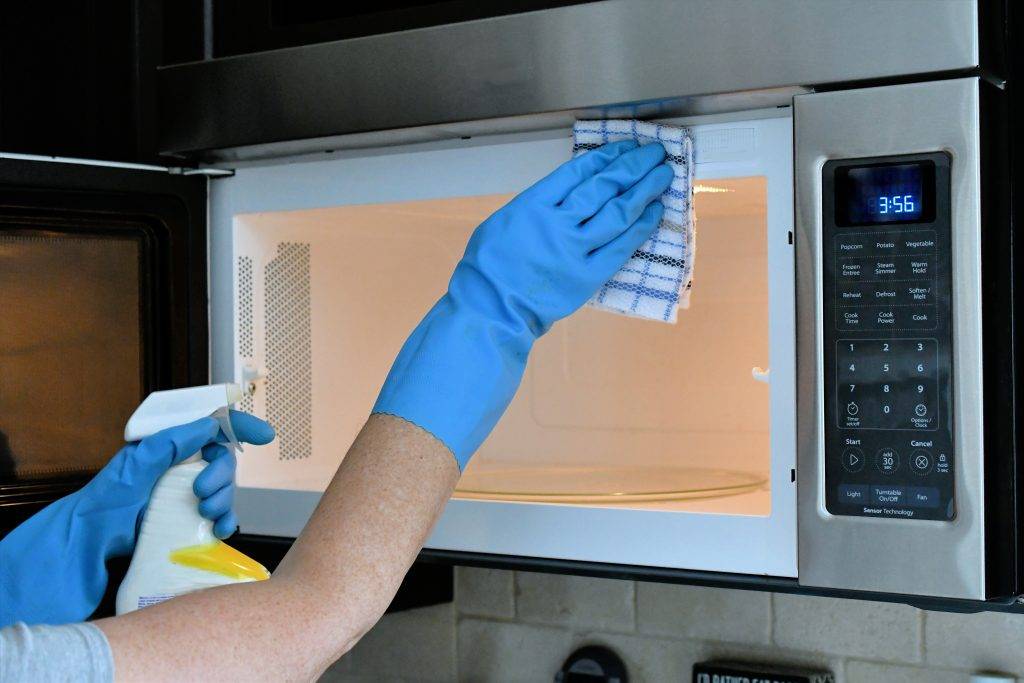 Doing housework chores by cleaning the microwave in the kitchen