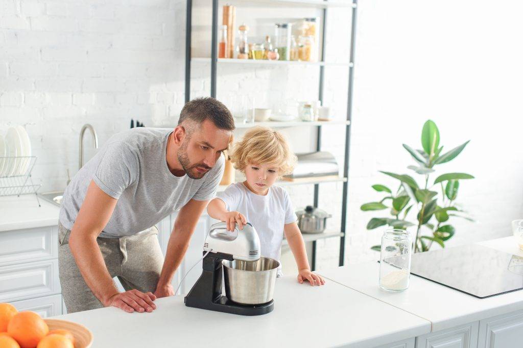 father watching how his son using mixer for making dough at kitchen