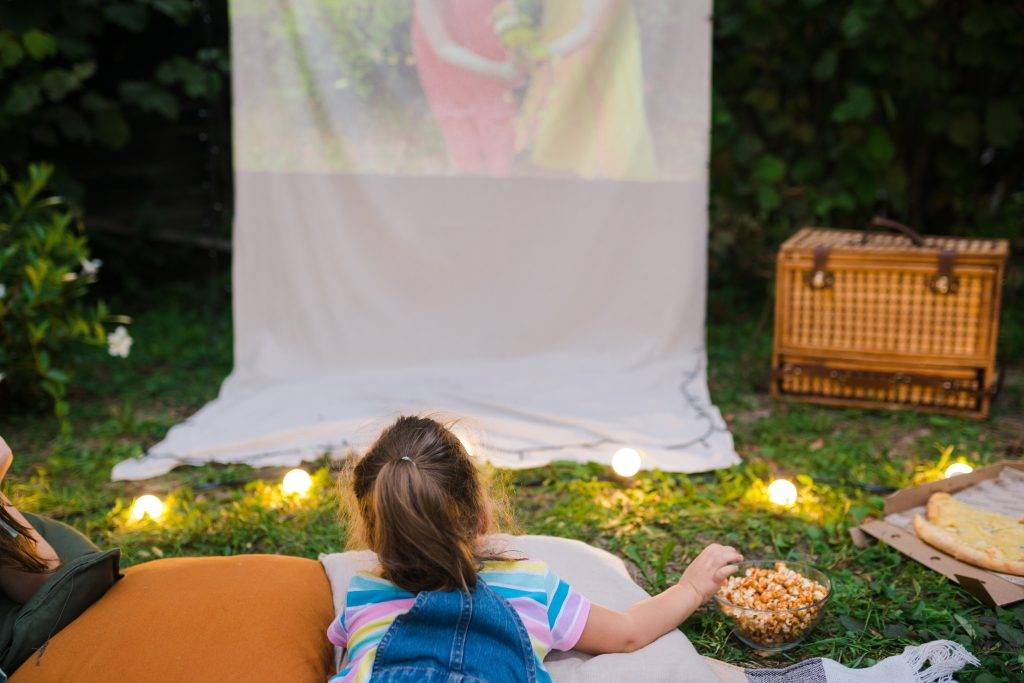 girl lying on the grass watching movie on projector in the backyard