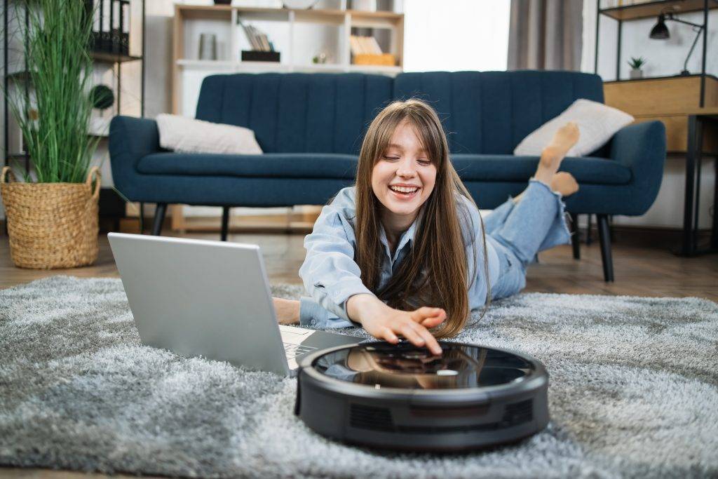 Happy woman using robot vacuum cleaner for chores