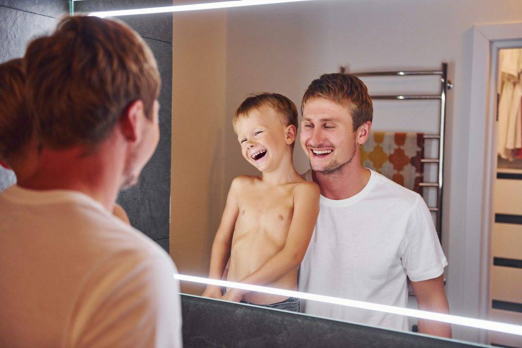 Looking in the mirror in bathroom. Father and son is indoors at home together