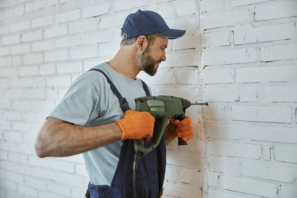 Male builder drilling wall with hammer drill