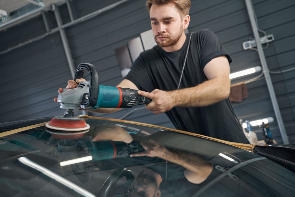Man polishing car with power buffer machine in automobile repair
