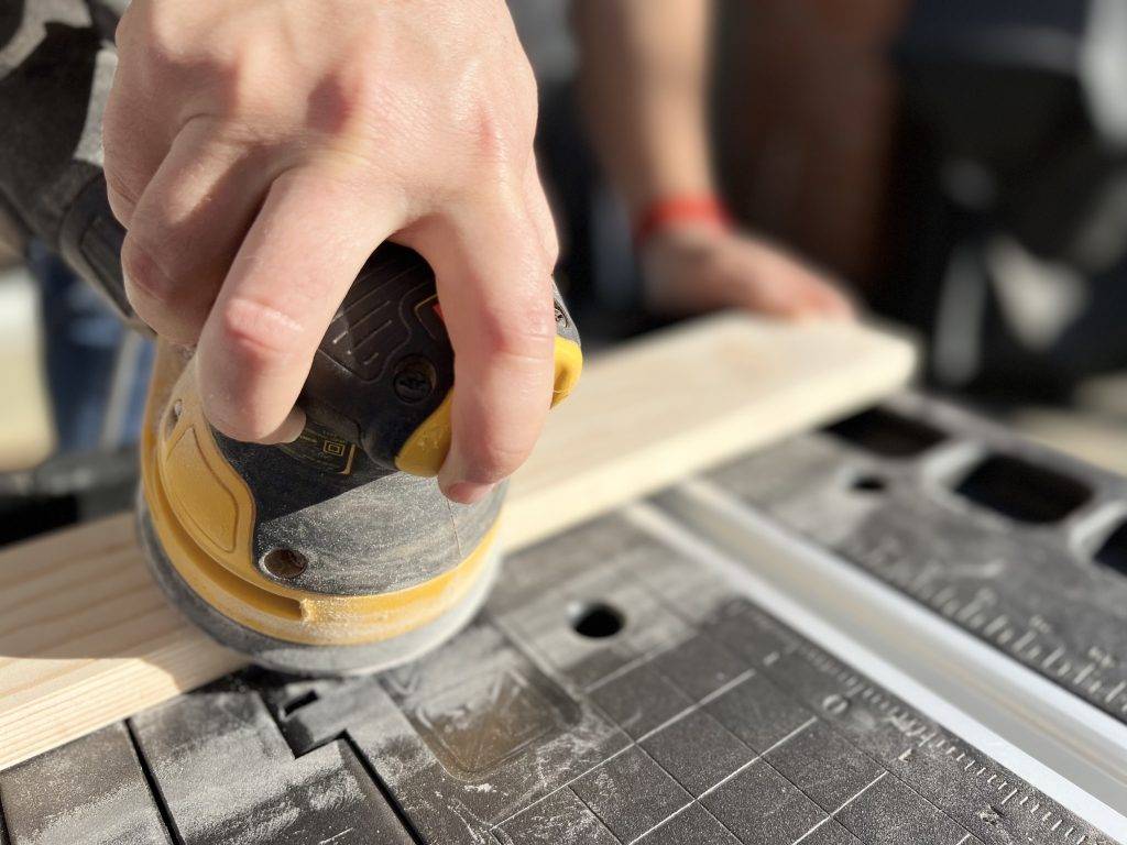 Sanding wood using an orbital wood sander on a workbench