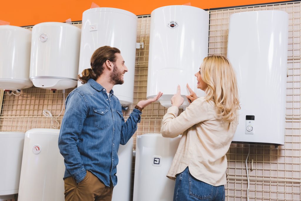 smiling boyfriend pointing with hand and girlfriend pointing with fingers at boiler in home