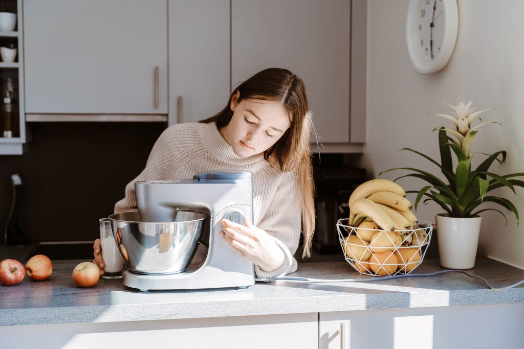 Teenager girl using mixer or food processor making dough. Child cooking at modern kitchen