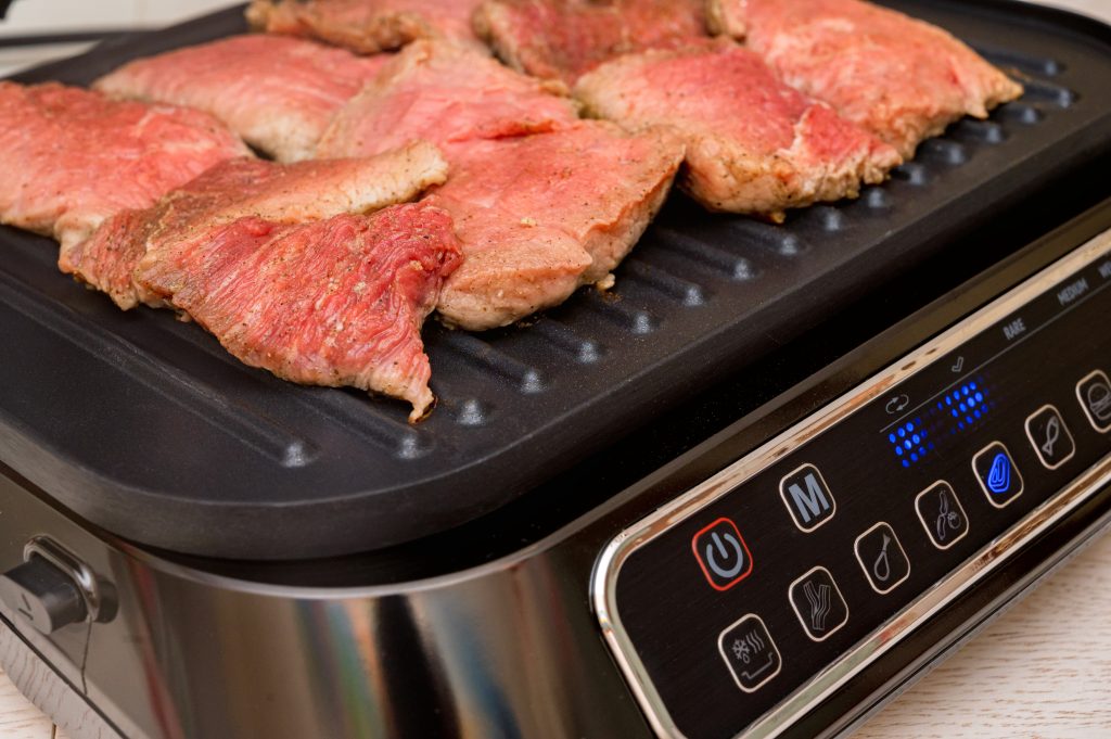 The process of cooking pork meat on electric grill close-up