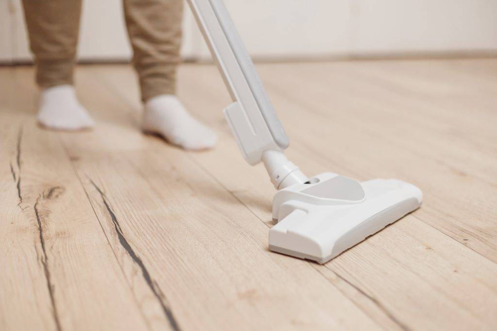 Woman Cleaning Wooden Floor With Wireless Vacuum Cleaner