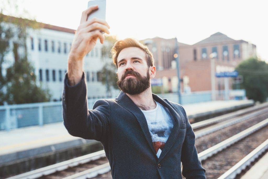 Young bearded man using smartphone taking selfie