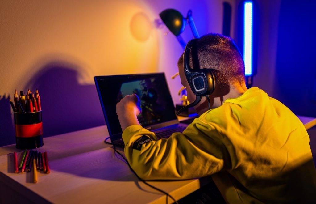 Young boy gamer with headphone playing video game on laptop at home.