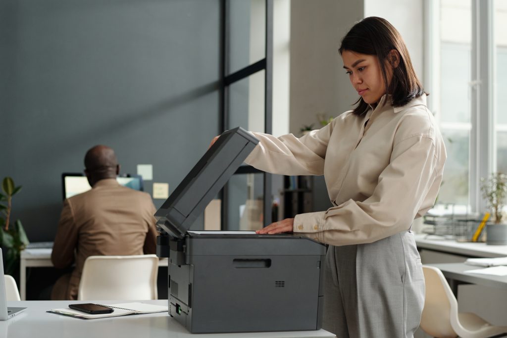 Young secretary or female office worker putting paper on scanning glass