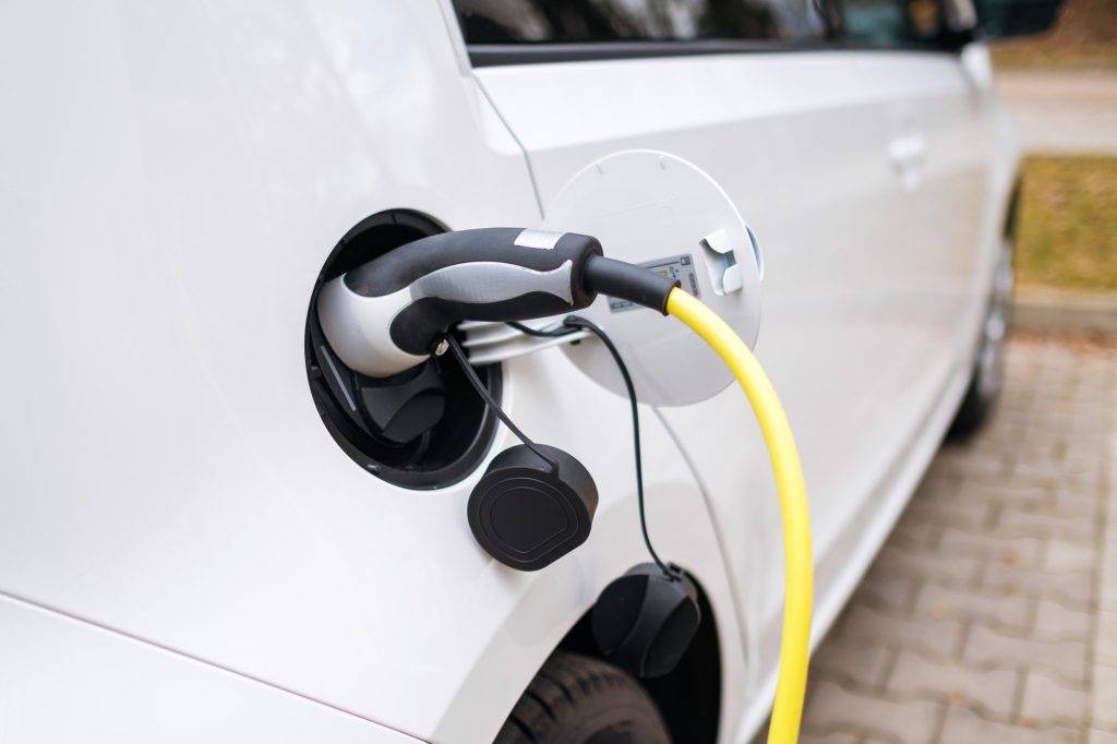 A white electric car charging at the charging station in the street