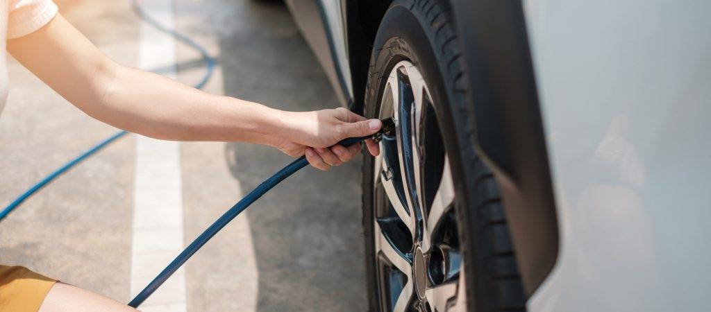 hand inflating tires of vehicle, checking air pressure and filling air on car wheel at gas station.