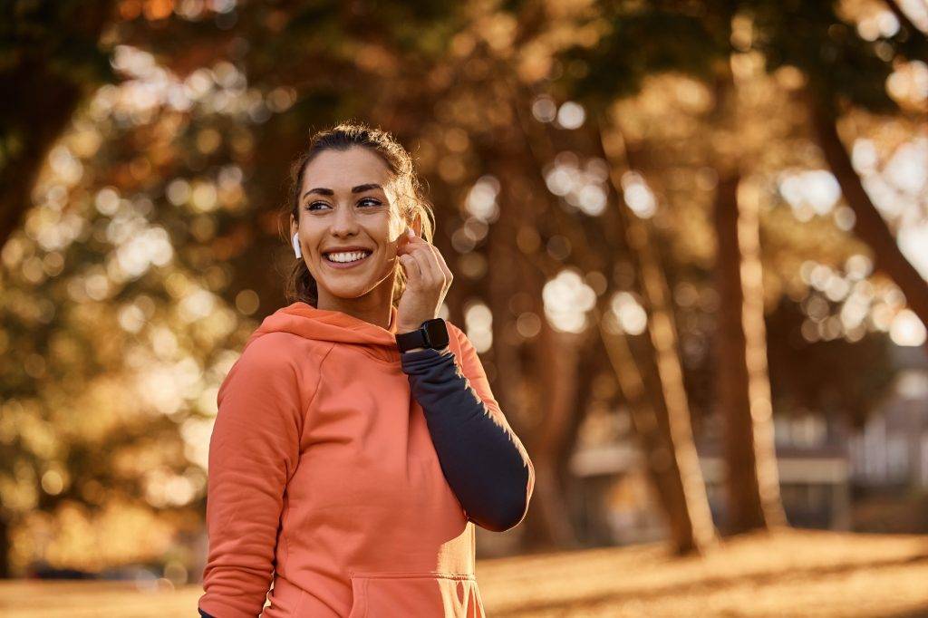 Happy athletic woman using earbuds while exercising in nature.
