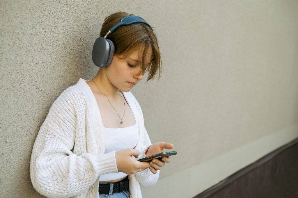 Headphones cradle a youth's ears, a phone serving as a vessel for their musical odyssey