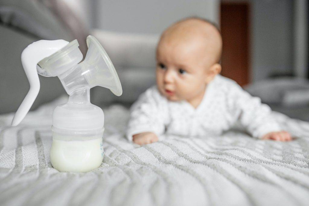 Child care concept. Breast pump with milk on background of small cute baby. Selective focus